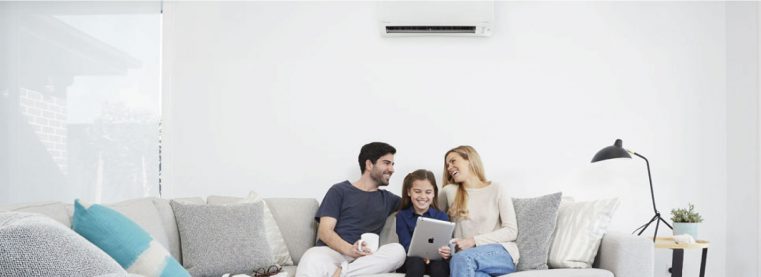 A family enjoying time together on a couch with a laptop and air conditioner nearby.
