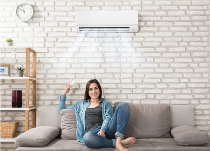 A woman sitting on a couch with an air conditioner, providing cool comfort on a hot day.